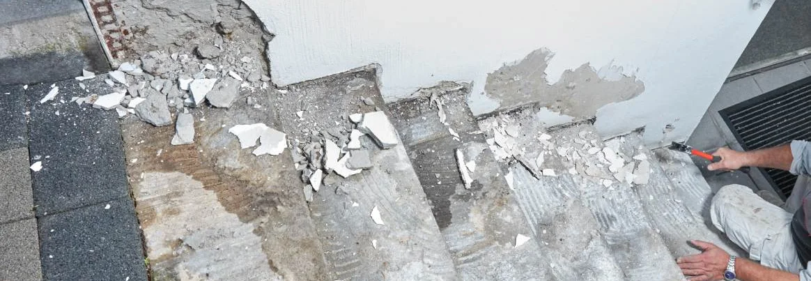 Eine Person saniert eine kaputte Betontreppe mit einem Werkzeug.